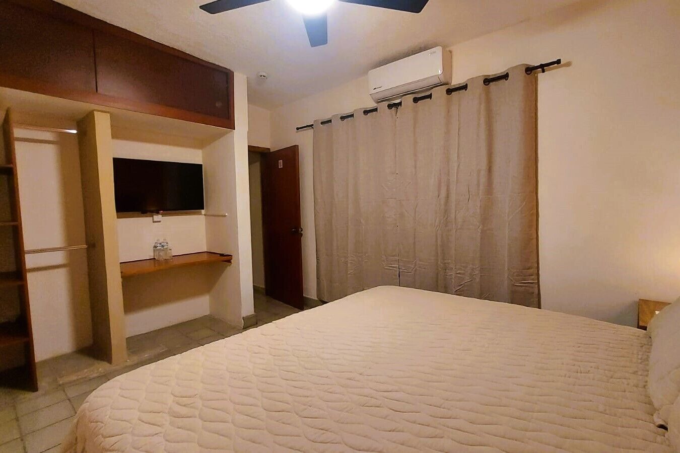Un dormitorio con una cama, televisión en un estante, armario y equipo de aire acondicionado.