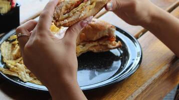 Una persona sostiene un sándwich sobre un plato negro sobre una mesa de madera.