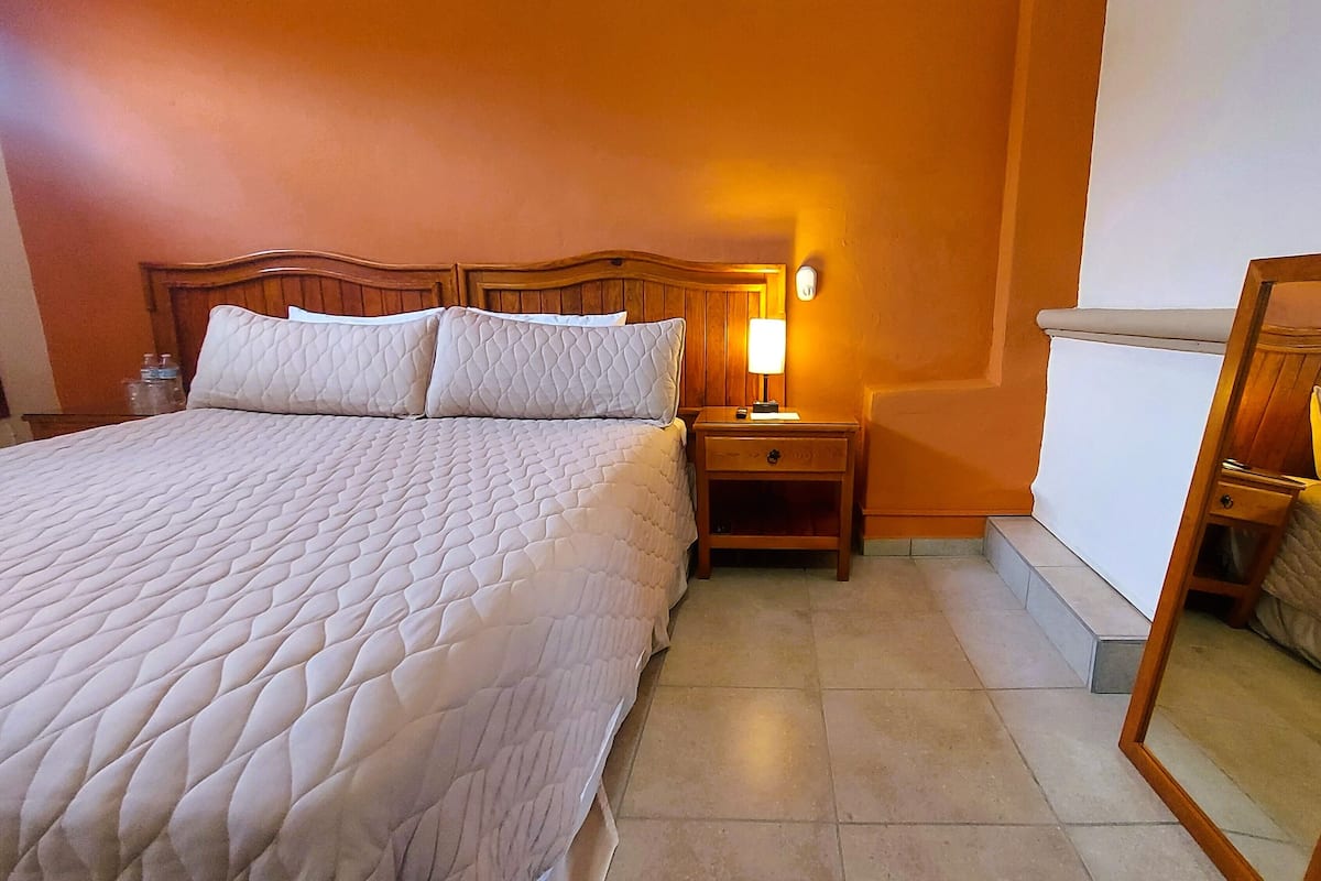 Quarto de hotel com cama grande, mesa de cabeceira com abajur e espelho.