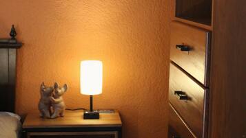 A corner of a room with an orange wall, a nightstand with a lamp, and a wooden cabinet.