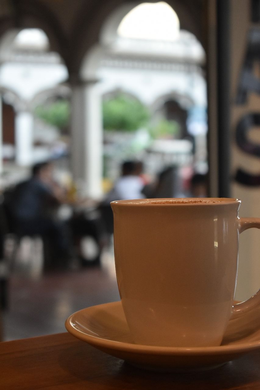 A coffee cup on a saucer in a cafe with a blurred background of people and arches.