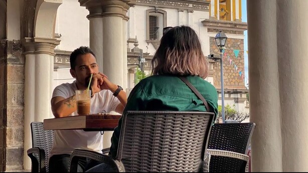 Two people sitting at an outdoor cafe with a view of a historic building with a yellow dome and a statue. - COMALITAS HOTEL Y CAFE (Comala)