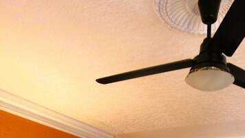 Un dormitori amb llit, una tauleta de nit, una commode i un ventilador de sostre.