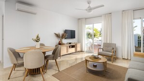 A modern living room with a dining table, chairs, a sofa, a TV, and a ceiling fan.
