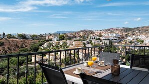 A balcony with a table set for breakfast, overlooking a residential area with houses and hills.