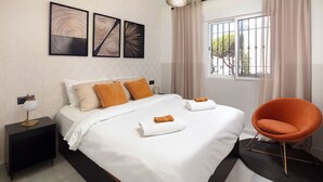 A modern hotel room with a large bed, two nightstands, a chair, and artwork on the wall.