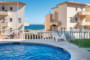 Ein Pool mit Blick auf das Meer, umgeben von weißen Stühlen und einem weißen Zaun.
