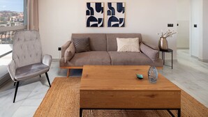 A modern living room with a sofa, armchair, and coffee table, featuring abstract wall art and a view of the city.