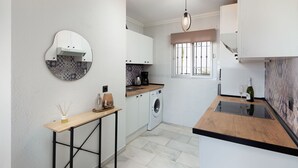 A modern kitchen with white cabinets, a round mirror, a washing machine, and a wine bottle.