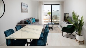 A modern living room with a dining area, a sofa with cushions, a TV, and a potted plant. - Olas Sunset by Alfresco Stays (Estepona)