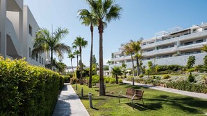 A pathway lined with palm trees and benches, leading to a modern building with balconies. - Olas Sunset by Alfresco Stays (Estepona)