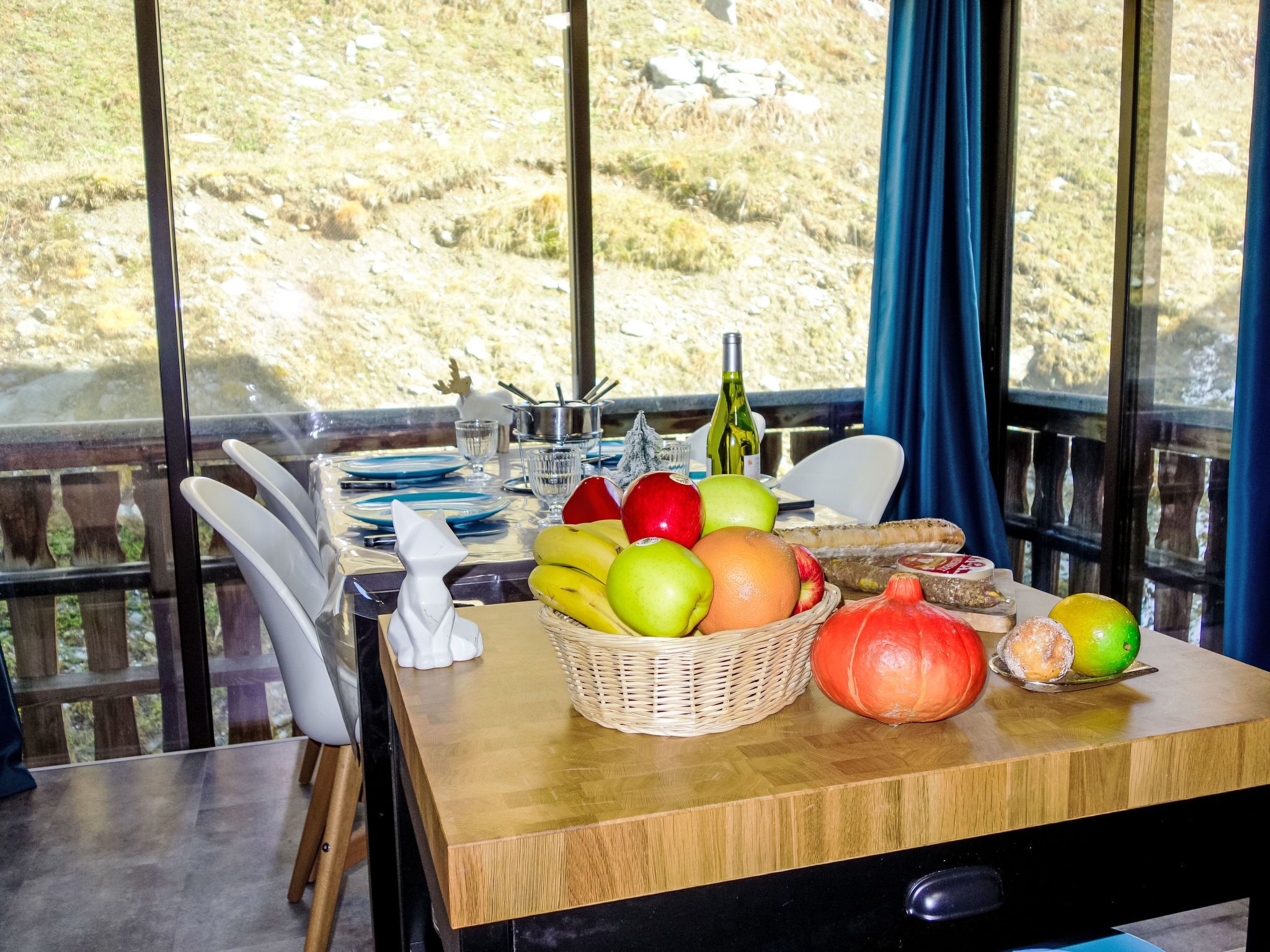 A dining table set with plates, a bottle of wine, and a basket of fruits.