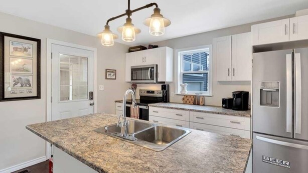 A modern kitchen with granite countertops, stainless steel appliances, and a farmhouse-style light fixture. - Courtland Heaven Retreats (Courtland)