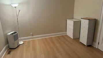 Una habitación con piso de madera, un calentador portátil, un aparador blanco y una lámpara de pie.