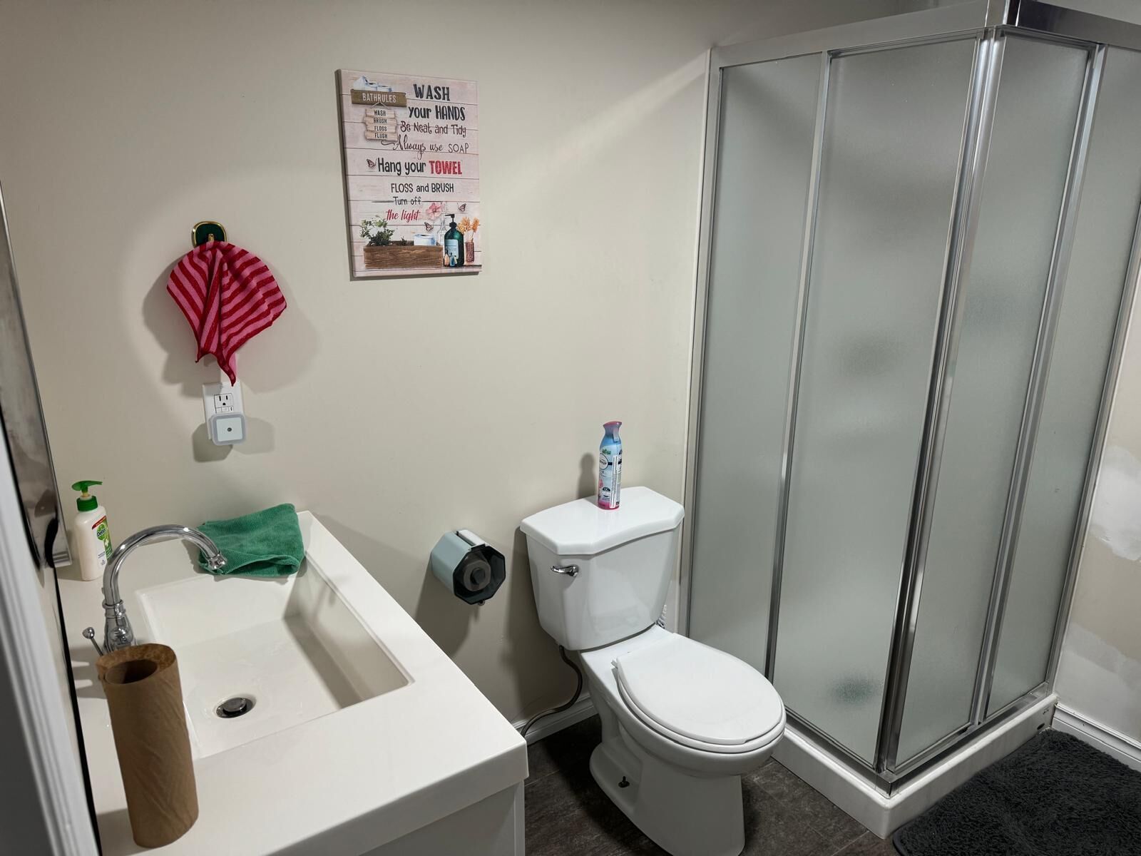Un baño con lavamanos, inodoro y ducha. Hay un cartel en la pared con normas del baño.