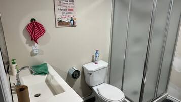 Un baño con lavamanos, inodoro y ducha. Hay un cartel en la pared con normas del baño.