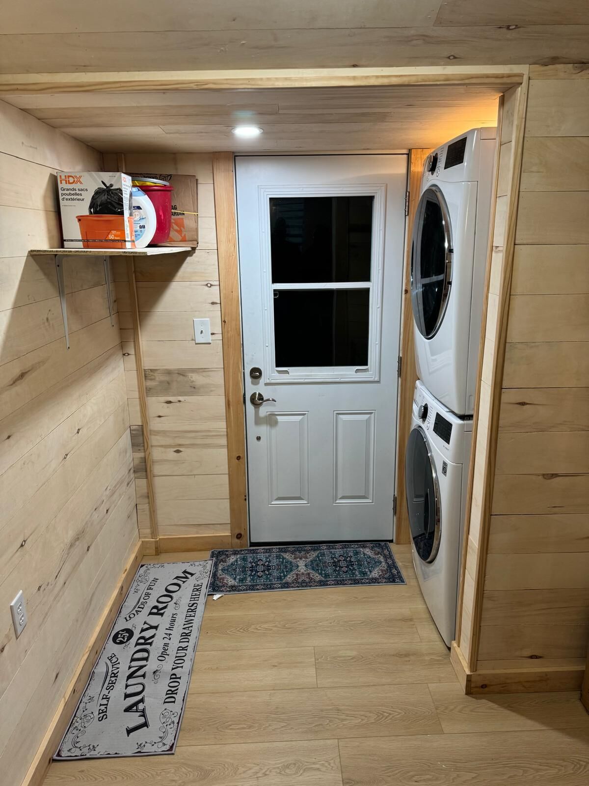 A laundry room with a washing machine, a door, and a shelf with cleaning supplies.