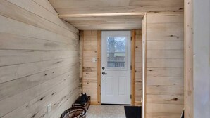 A wooden interior hallway with a white door, a small step leading to a porch, and a trash bin. - Courtland Heaven Retreats (Courtland)