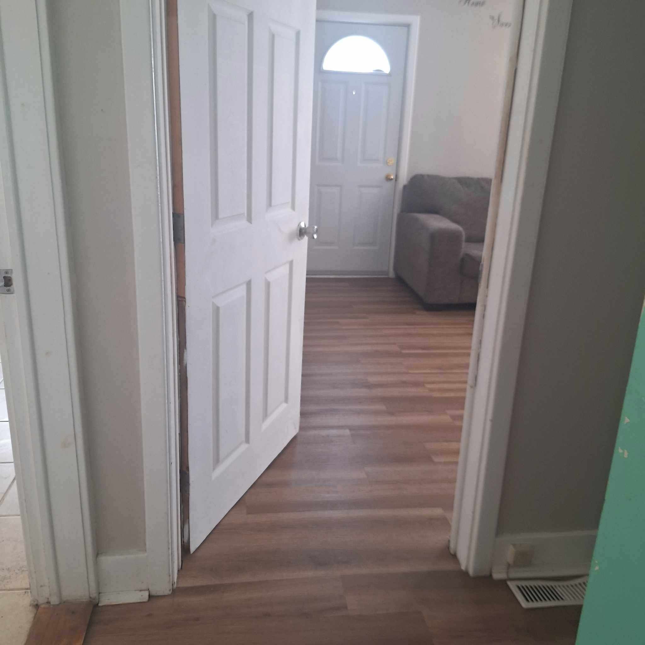 Un pasillo con piso de madera que conduce a una habitación con una puerta y un ventanal.