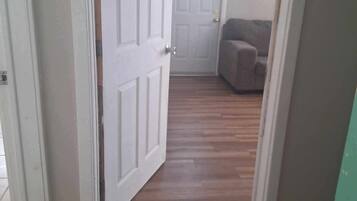 Un pasillo con piso de madera que conduce a una habitación con una puerta y un ventanal.