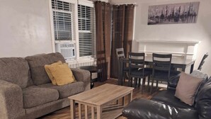 A living room with a grey sofa, a black leather sofa, a wooden coffee table, and a dining table with chairs.