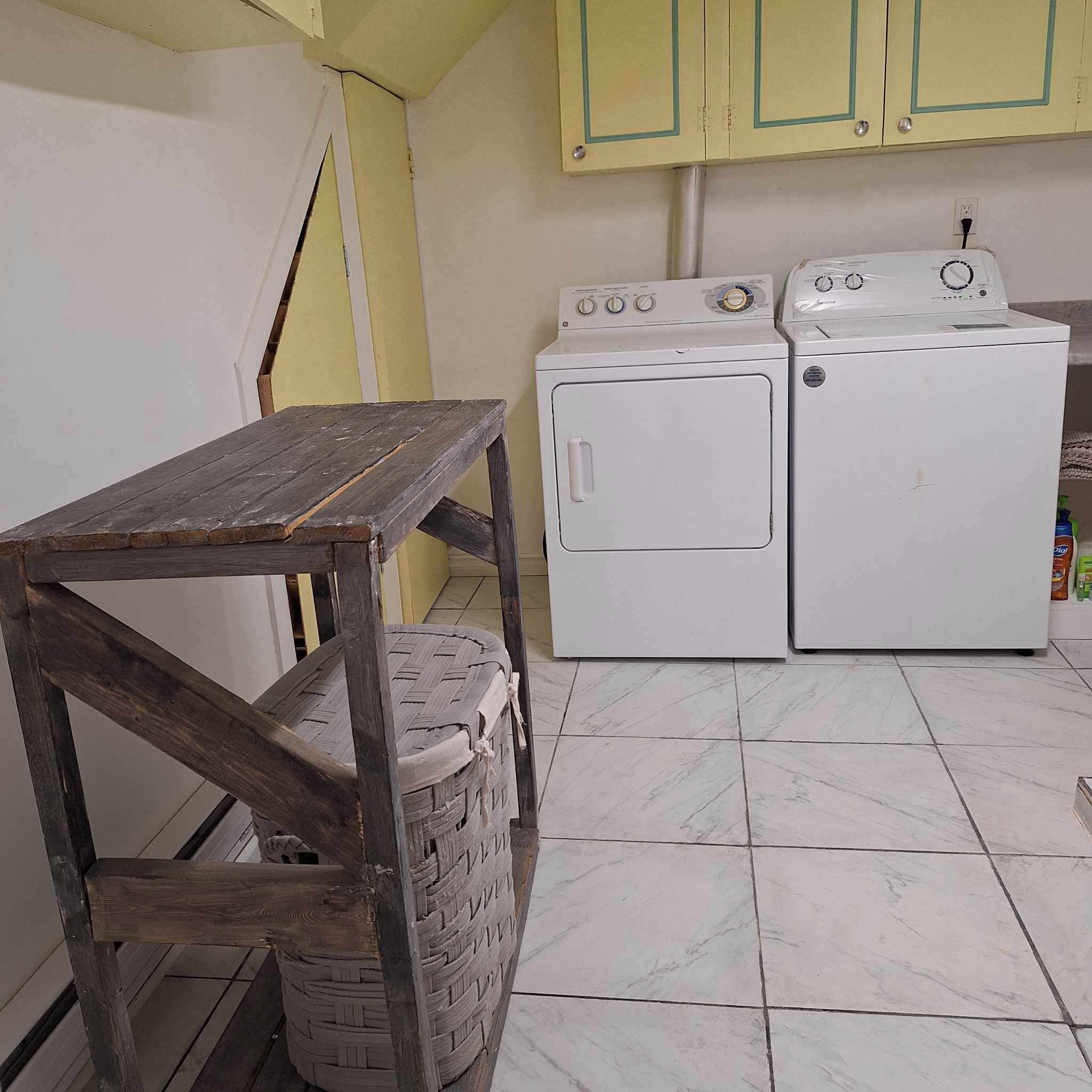 Een wasserette met twee witte wasmachines, een houten tafel en een geweven mand.