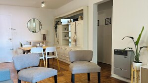 Una sala moderna con piso de madera, sofás tapizados en gris, una mesa de centro redonda y un comedor con una mesa y sillas blancas.