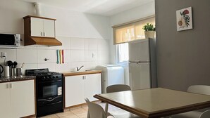 Cocina compacta con armarios blancos, estufa y comedor con mesa y sillas.