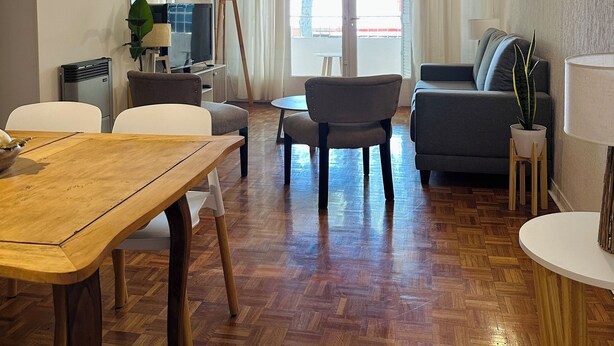 Una sala de estar moderna con una mesa de comedor de madera, un sofá gris y una mesita auxiliar con una lámpara.