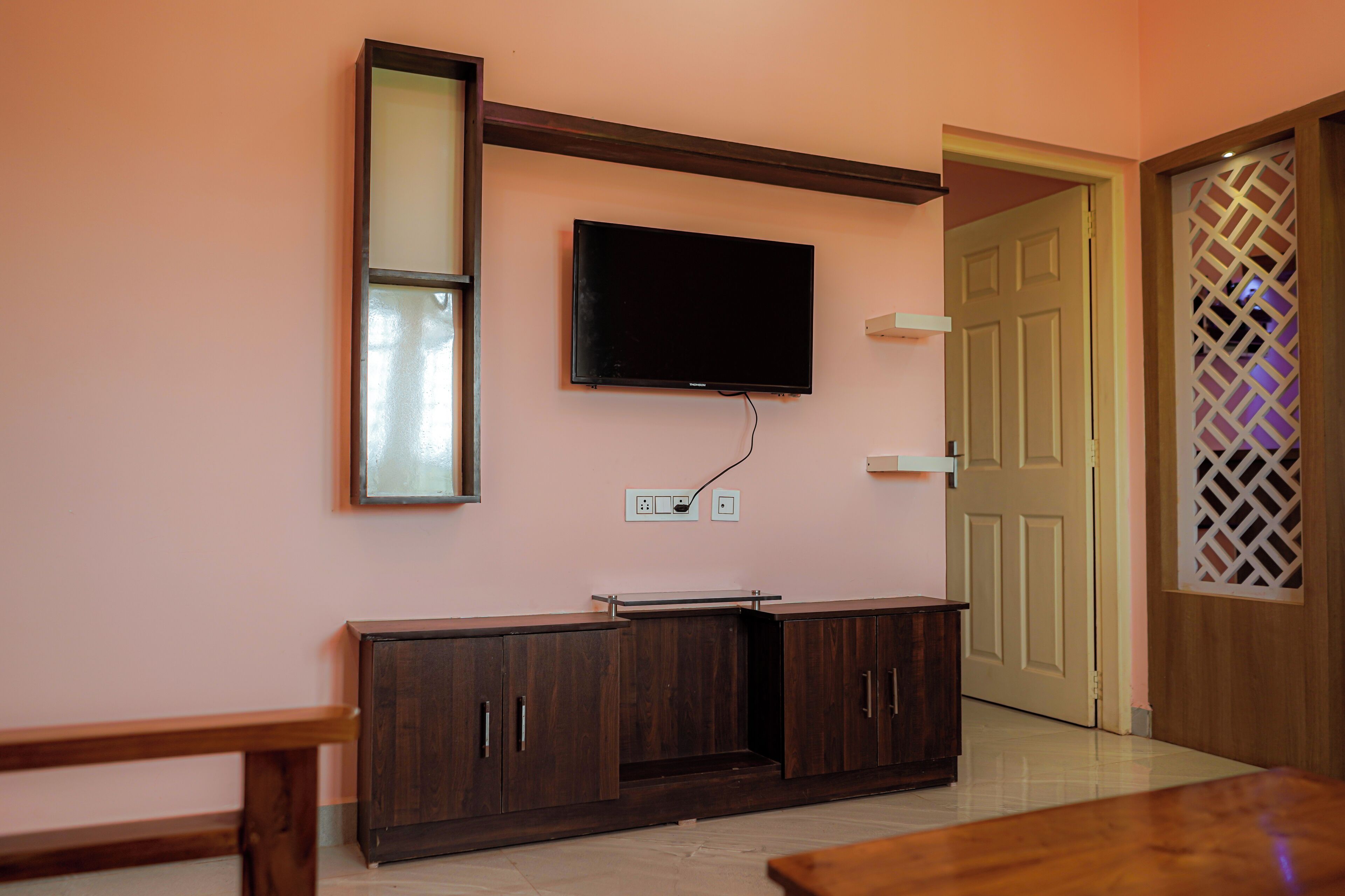 A room with a TV mounted on the wall, a wooden cabinet, and a door with a lattice design.