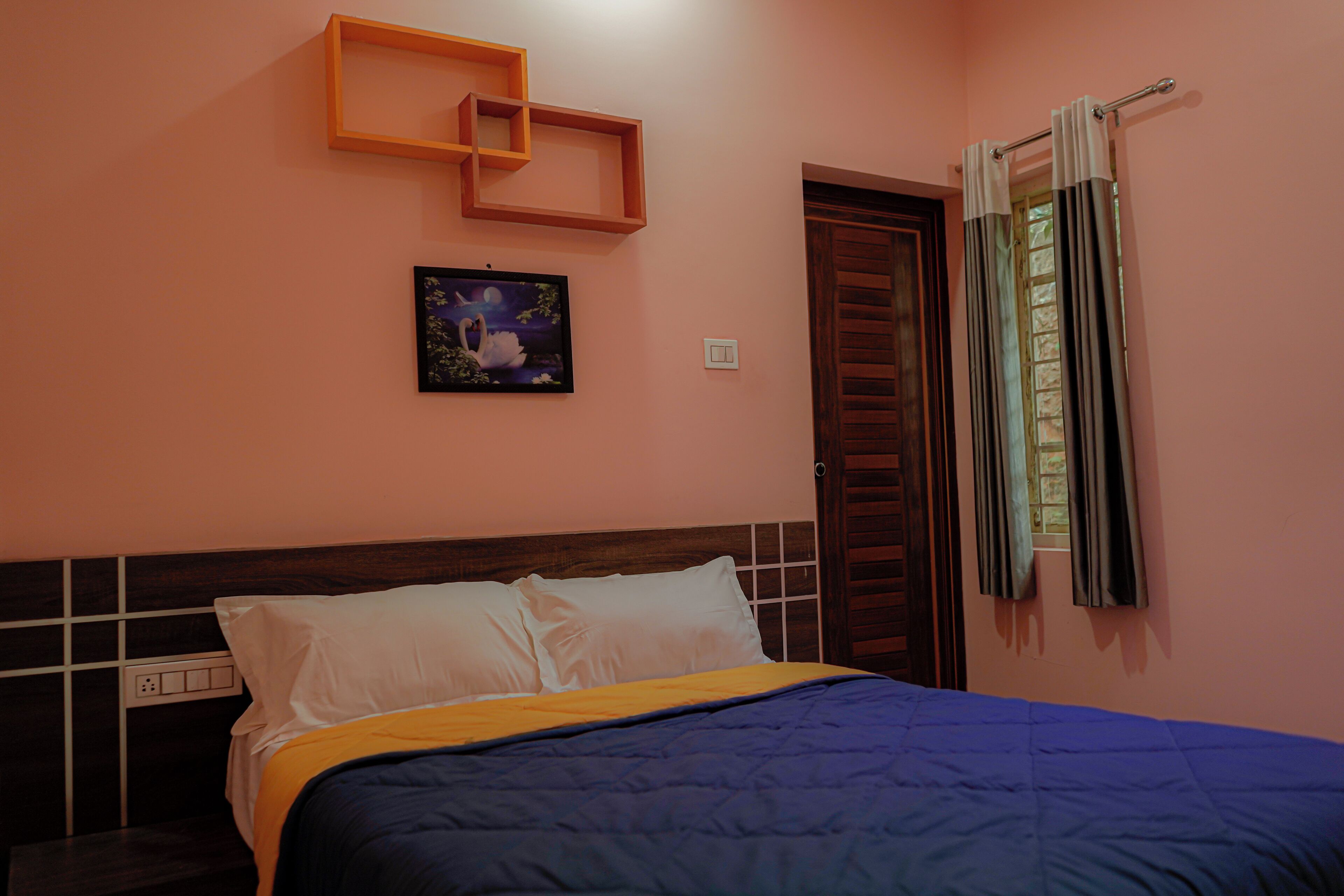 Una camera da letto con un letto, un comodino, una mensola a parete, un quadro e una finestra con tende.