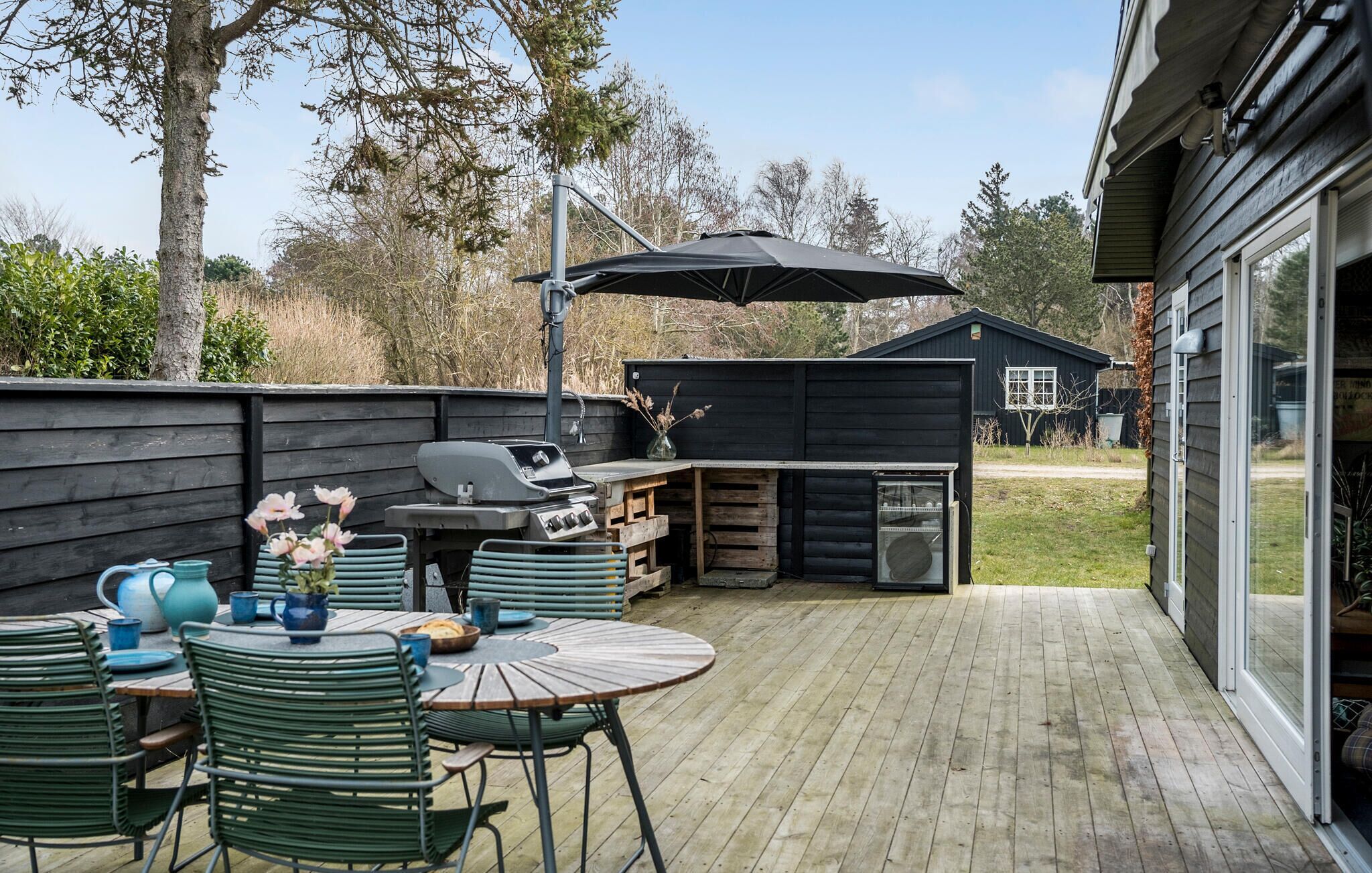 A deck with a grill, outdoor table, chairs, and a small shed.