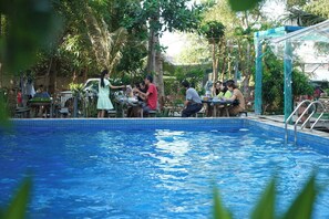 A poolside area with tables and chairs, surrounded by greenery and a covered seating area. - Stop And Go Lang Chai Bau Trang (Bac Binh)