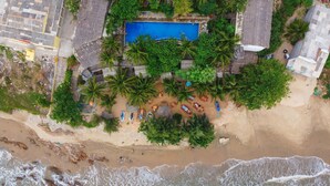 Vue aérienne d’un complexe hôtelier doté d’une piscine entourée de palmiers et de chaises de plage.