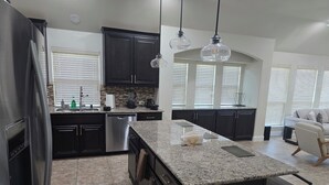 A modern kitchen with dark cabinets, granite countertops, a stainless steel refrigerator, and a central island with a built-in sink.