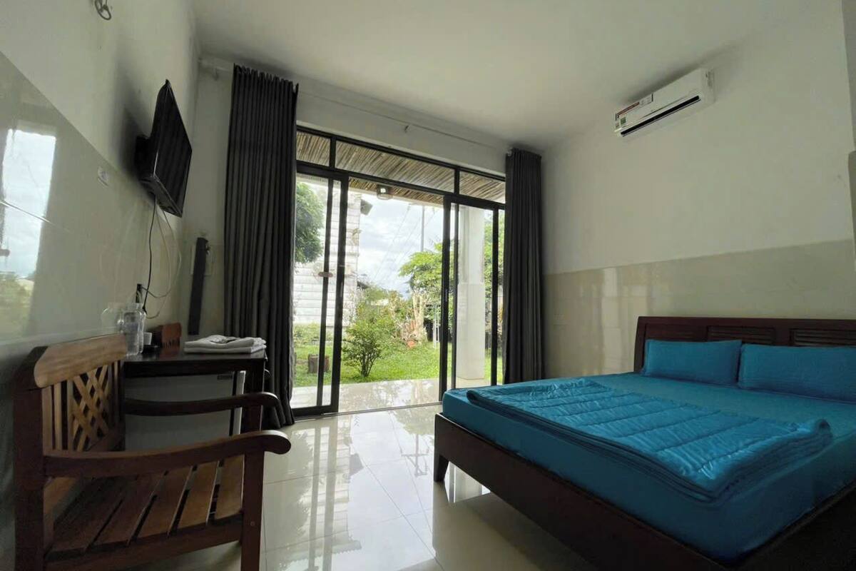 Habitación de hotel con cama, escritorio, silla y vistas al exterior a través de amplias ventanas.
