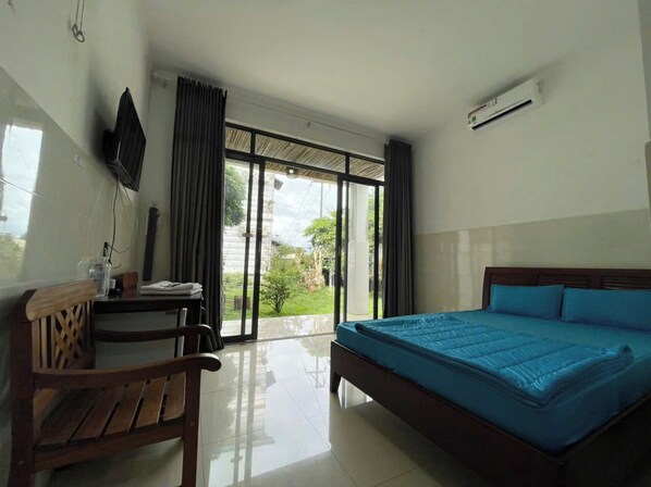 A hotel room with a bed, a desk, a chair, and a view of the outdoors through large windows.