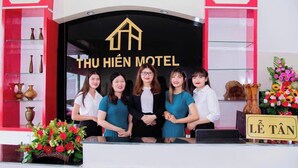 A reception desk at Thái Hến Motel with a black sign, a group of people standing behind it, and a vase of flowers on the left. - Thu Hien Hotel Pleiku - by BAY LUXURY (Gao)