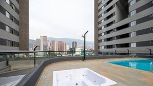 Ein Poolbereich auf dem Dach mit Whirlpool, umgeben von modernen Gebäuden und einer Stadtlandschaft im Hintergrund.