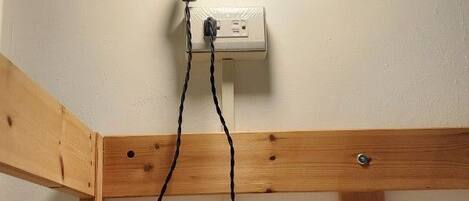 Un rincón de una habitación con un banco de madera, un aplique de pared y un enchufe.