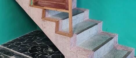 Una escalera con barandilla de madera y una puerta roja que da a una habitación con paredes verde azulado y piso de baldosas.