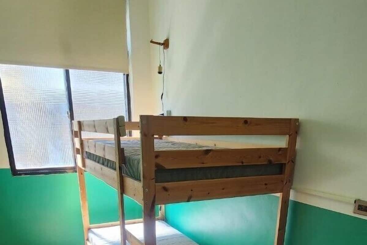 A bunk bed with a wooden frame and a red cushion, a red sofa, and a herringbone-patterned wooden floor.