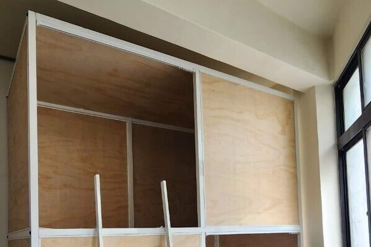 A room with a built-in wooden wardrobe, a white ladder, and a herringbone-patterned wooden floor.
