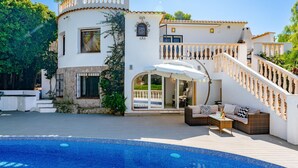 Eine moderne Villa mit Swimmingpool, Sitzgelegenheiten im Freien und einer Treppe, die zu einem Balkon führt.