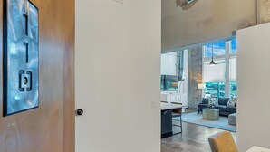 A modern interior with a wooden door, a white wall with a power outlet, a kitchen area with a dining table, and a large window. - Hebrews 13:2- Wonderful 2 bedroom condo downtown Waco, Baylor, Silos (Waco)