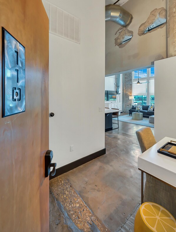A modern interior with a wooden door, a white wall with a power outlet, a kitchen area with a dining table, and a large window. - Hebrews 13:2- Wonderful 2 bedroom condo downtown Waco, Baylor, Silos (Waco)