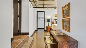 A hallway with a wooden floor, a glass-top table with books, a lamp, and framed pictures on the wall. - Hebrews 13:2- Wonderful 2 bedroom condo downtown Waco, Baylor, Silos (Waco)