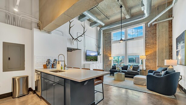 A modern kitchen with a large island, a dining area with a sofa and coffee table, and a large window with a view of the outdoors. - Hebrews 13:2- Wonderful 2 bedroom condo downtown Waco, Baylor, Silos (Waco)