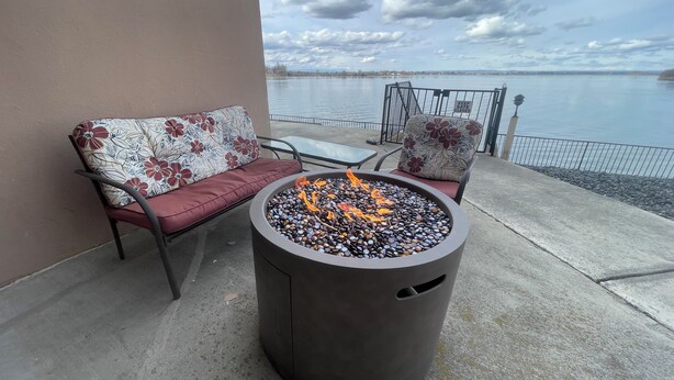 Une terrasse avec un foyer, deux canapés ornés de coussins à motifs floraux et une vue sur une étendue d’eau.