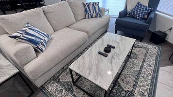 Un soggiorno con un divano beige, una poltrona blu, un tavolino da caffè in marmo e un tappeto decorato.